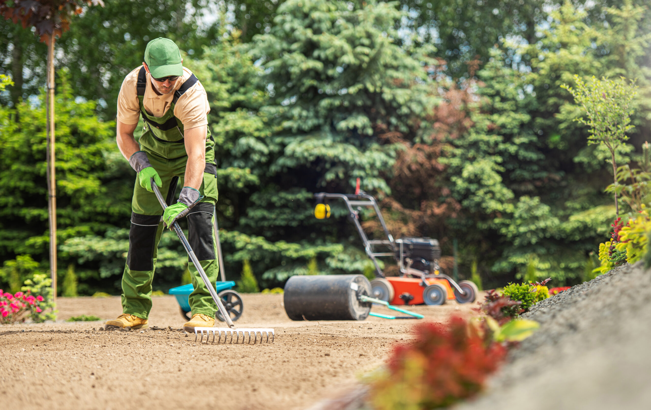 Caucasian Garden Specialist with Rake Preparing Soil For Natural Grass Turfs Installation. Landscaping Theme.